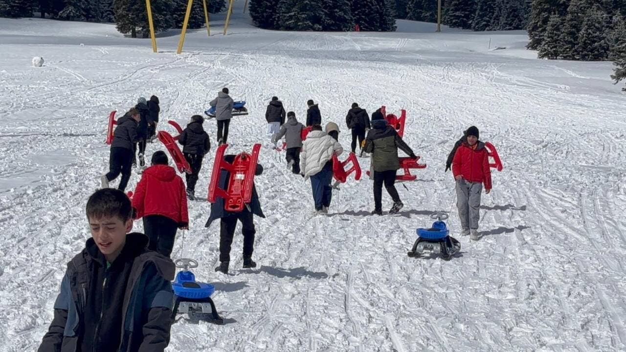 Uludağ'da nisan ayında karın keyfini çıkaran çocuklar ve günübirlikçiler kızaklarıyla kayıyor.